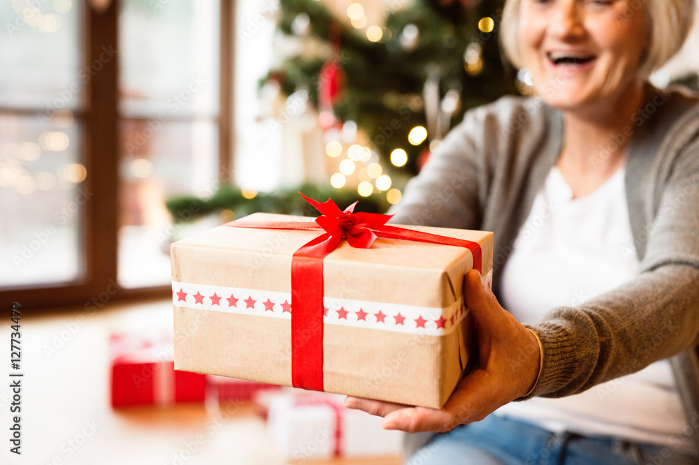 Unrecognizable senior woman in front of Christmas tree giving gi