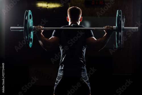 Man training squats with barbells over head.
