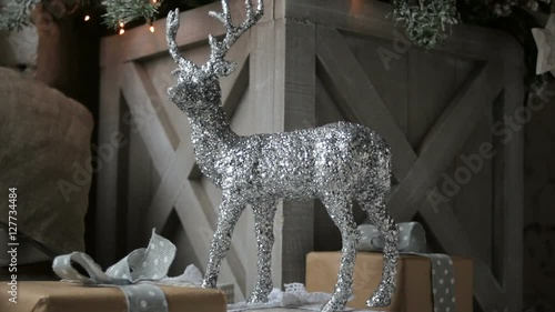 the silver shiny reindeer stands on the toy gifts at the Christmas tree