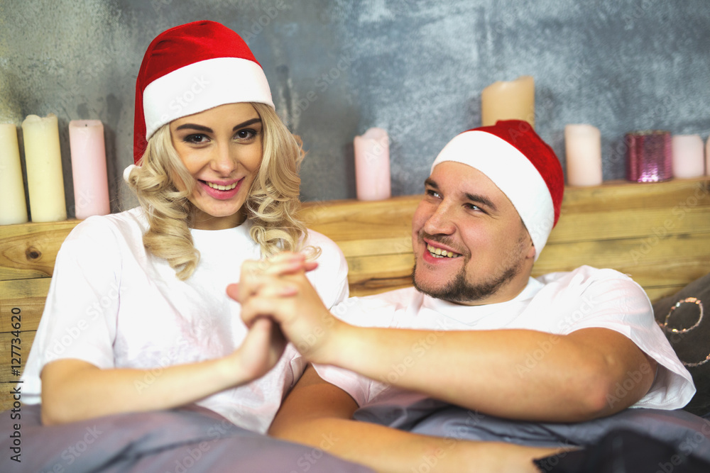 Fototapeta premium Christmas. New Year. Man and woman in Christmas hats lie in bed, they smile it fun. Close-up