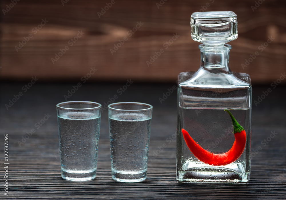 selectiv focus glasses of cold vodka with chili peppers  on wood