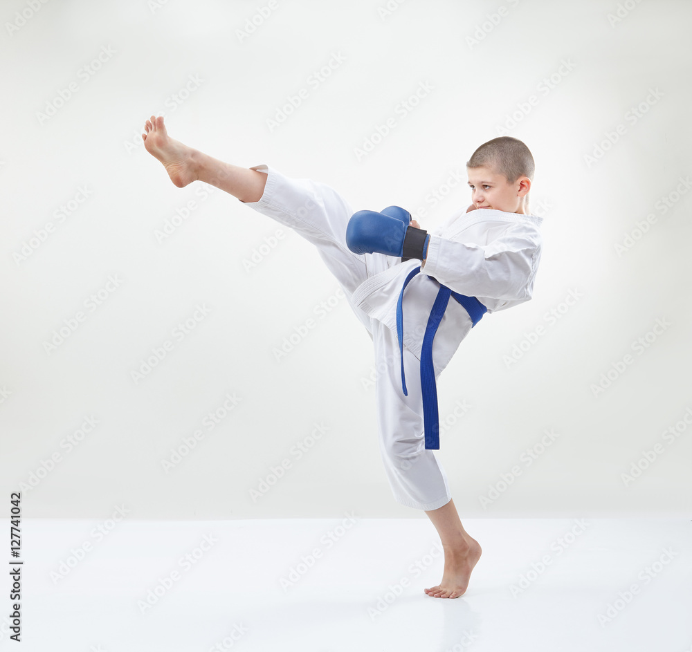 Boy in karategi and blue overlays on hands beats a kick leg Boy in karategi and blue overlays on hands beats a kick leg