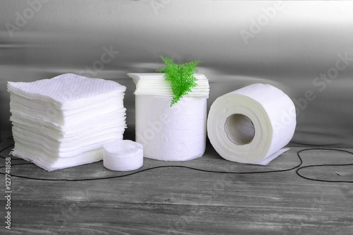 White paper towel, toilet paper, paper tissues, cotton disks on wooden table.	Kitchen disposables, toiletries. Toned image.