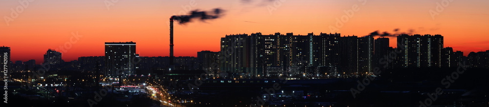 Panorama of a large industrial city and high-rise buildings on the background of bright orange sunset sky.