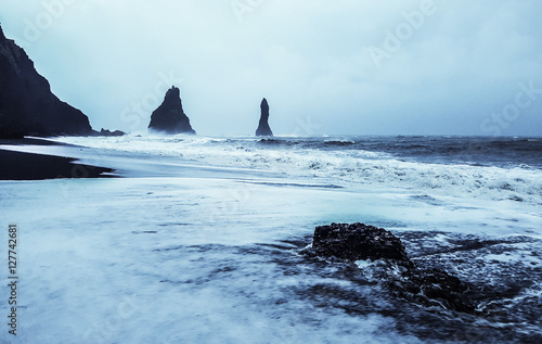 Rock formation on black volcanic beach at Cape Dyrholaey, South Iceland, with mount Reynisfjall on the background © donvictori0