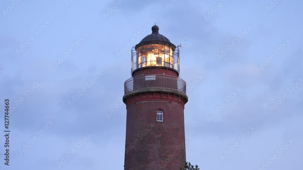 Shinning old lighthouse above pine forest after sunset. Tower illuminated with strong warning light. Lighthouse built from red bricks, gallery with iron handrail around glass cover of spotlight. Shinning old lighthouse above pine forest after sunset. Tower illuminated with strong warning light. Lighthouse built from red bricks, gallery with iron handrail around glass cover of spotlight.