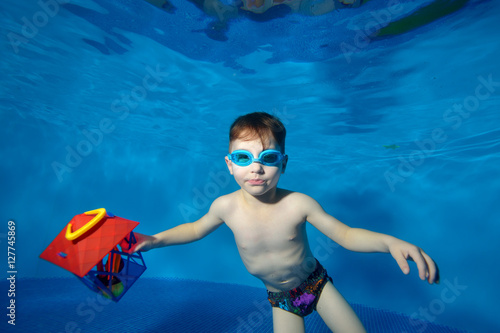 Little boy swims underwater in the pool with a Christmas toy in hand and looking at me. Portrait. Shooting underwater. Landscape orientation