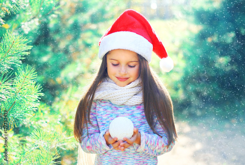 Christmas child little girl in santa red hat holding snowball ne