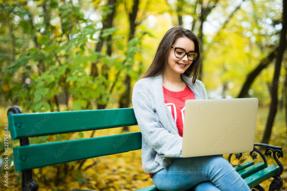 Young happy girl students working on laptop in autumn park Young happy girl students working on laptop in autumn park