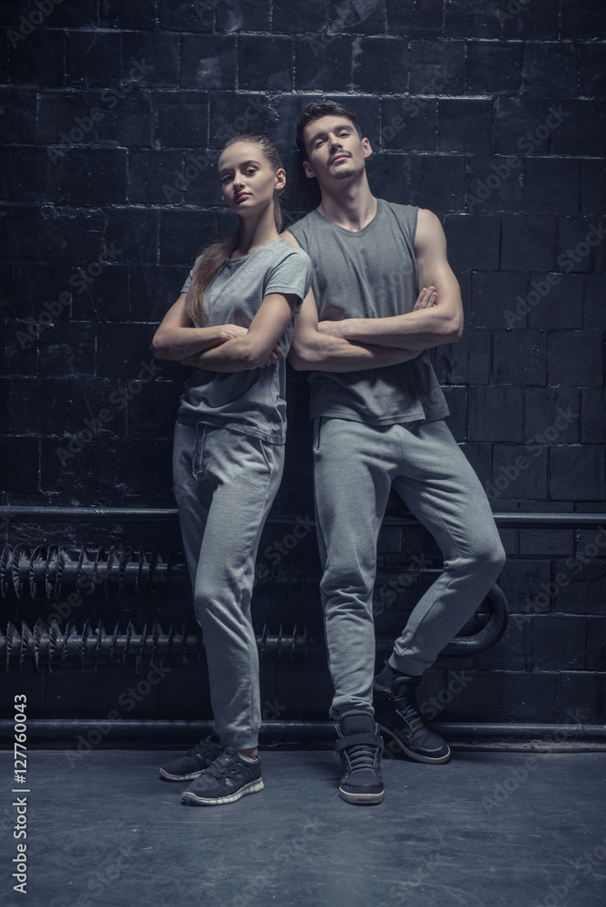 Concentrated dancers standing near the black wall with crossed arms