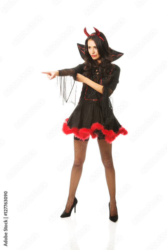 Full length woman wearing devil clothes pointing to the corner