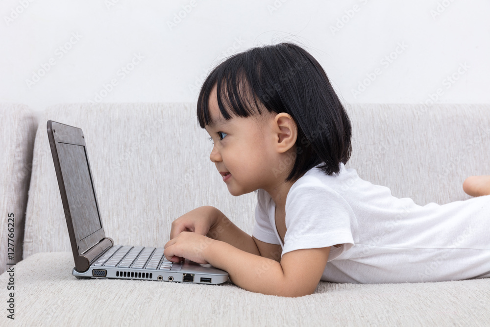 Asian Chinese little girl laying on sofa using laptop Asian Chinese little girl laying on sofa using laptop