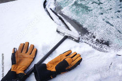 removing snow and ice on the car windshield with gloves, ice scraper and broom