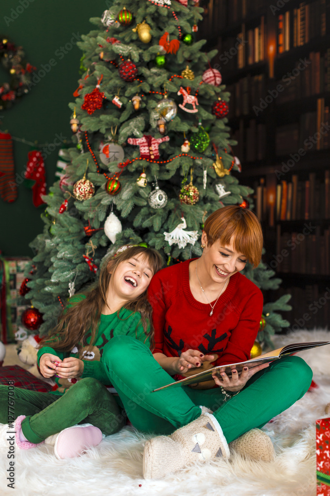 Mother with her daughter reading the book near dressed up christmas tree Mother with her daughter reading the book near dressed up christmas tree