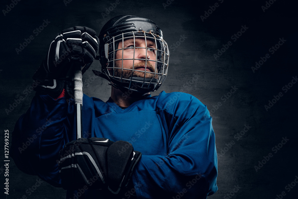 Fototapeta premium A bearded ice-hockey player in safety helmet holds the gaming st