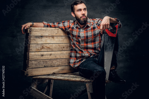 A man in a red plaid shirt, sits on a wooden box and holds hands