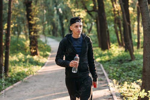 Handsome young man walking with plastic bottle. Attractive guy going in forest. Evening relaxation, tourism, hiking concept