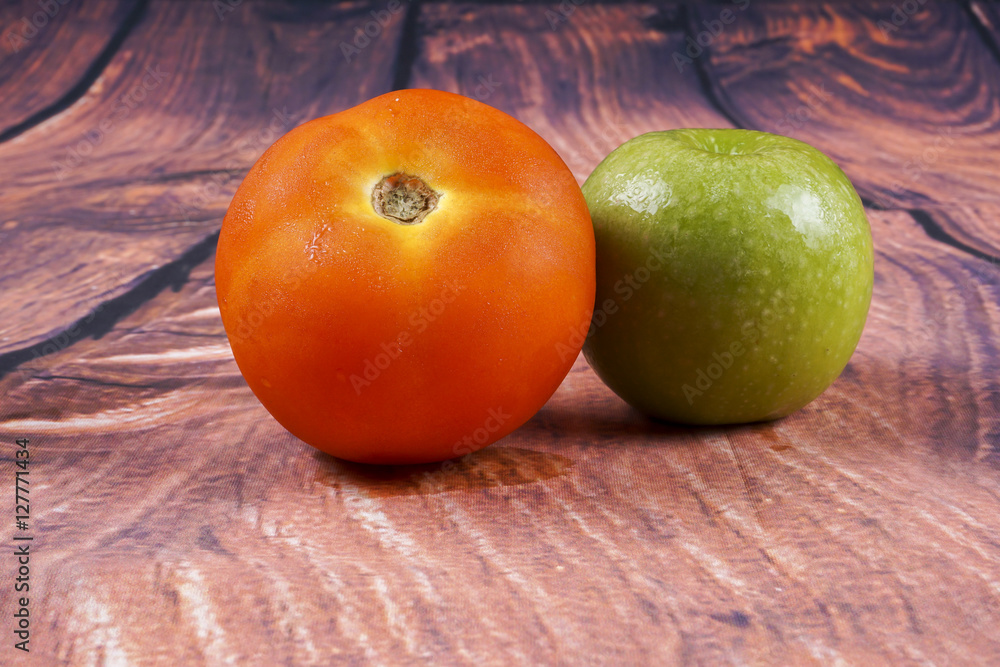 Tomato and green apple on wooden background.
