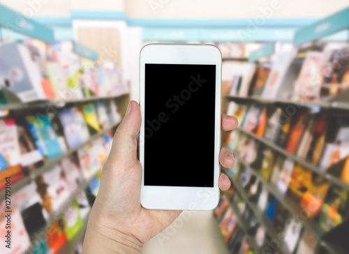 Hand holding mobile smart phone on blur Background of book and b