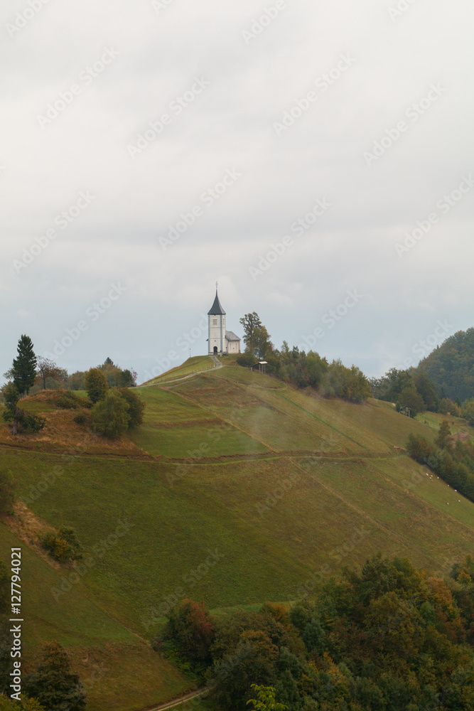 Jamnik church on a hillside in autumn, foggy weather at sunset in Slovenia