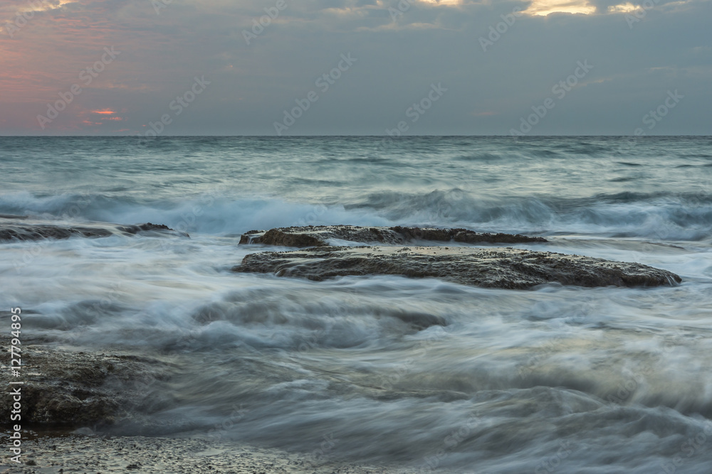 Rocks surrounded by silky waves water after sunset