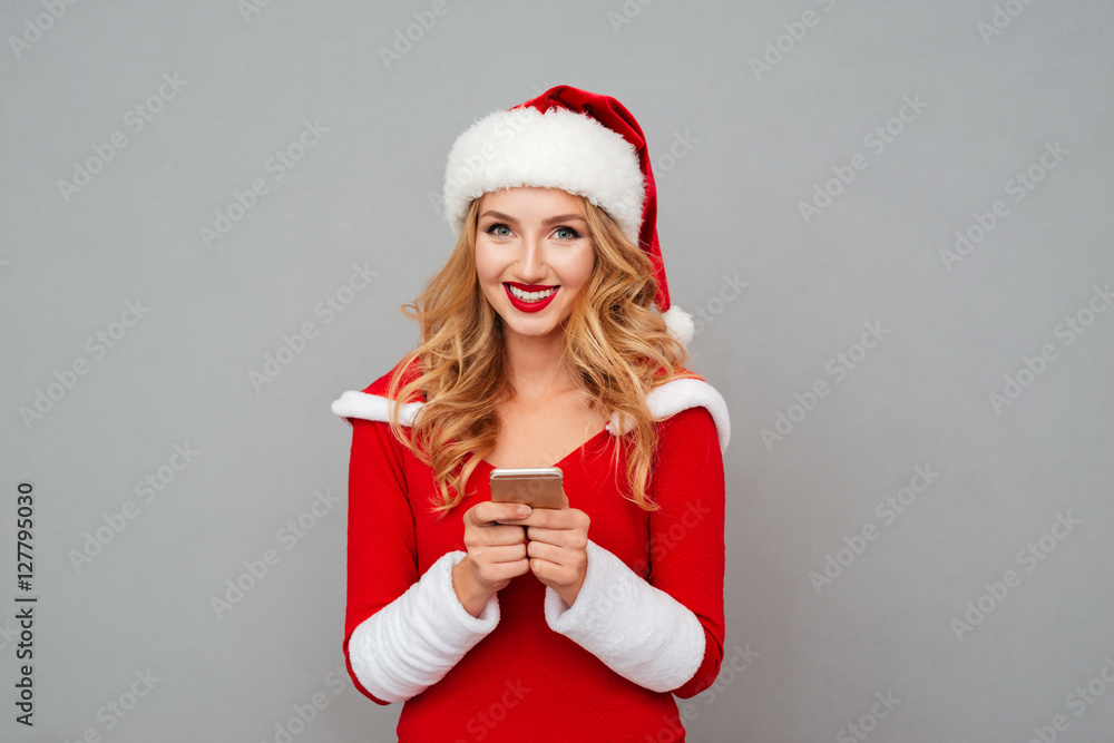 Cheerful pretty young woman in santa costume using mobile phone Cheerful pretty young woman in santa costume using mobile phone