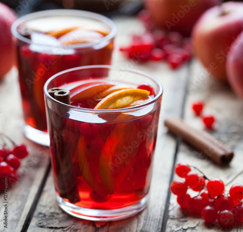 Closeup of mulled wine or sangria with orange and apple slices, cranberries, cinnamon, anise on wooden table. Square format