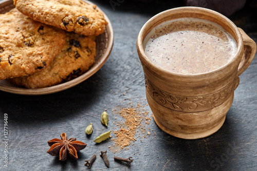 Masala tea chai latte traditional hot Indian sweet milk spiced drink, teh tarik, ginger, cinammon sticks, fresh spices blend, anise organic infusion healthy wellness beverage in rustic clay cup