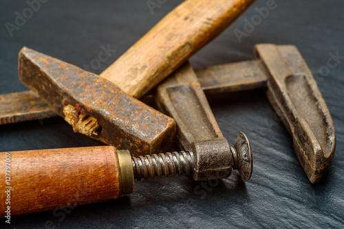 Old and well used handmade square hammer with short wooden handle and hand screw clamp on dark background.