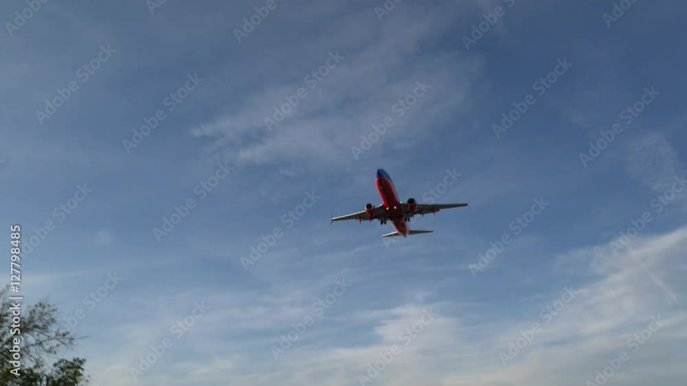 Low angle view of red airplane flying from airport after takeoff at the sunny summer day Low angle view of red airplane flying from airport after takeoff at the sunny summer day