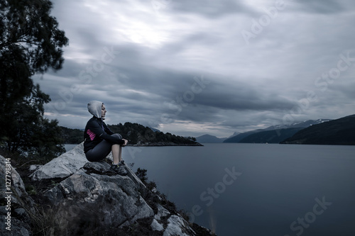 Young woman is sitting on the rocks near by fjord, Norway