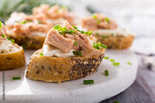 Slices of baguette with fresh tuna, cream cheese and chopped onion chives on marble board. Christmas themed dinner table.