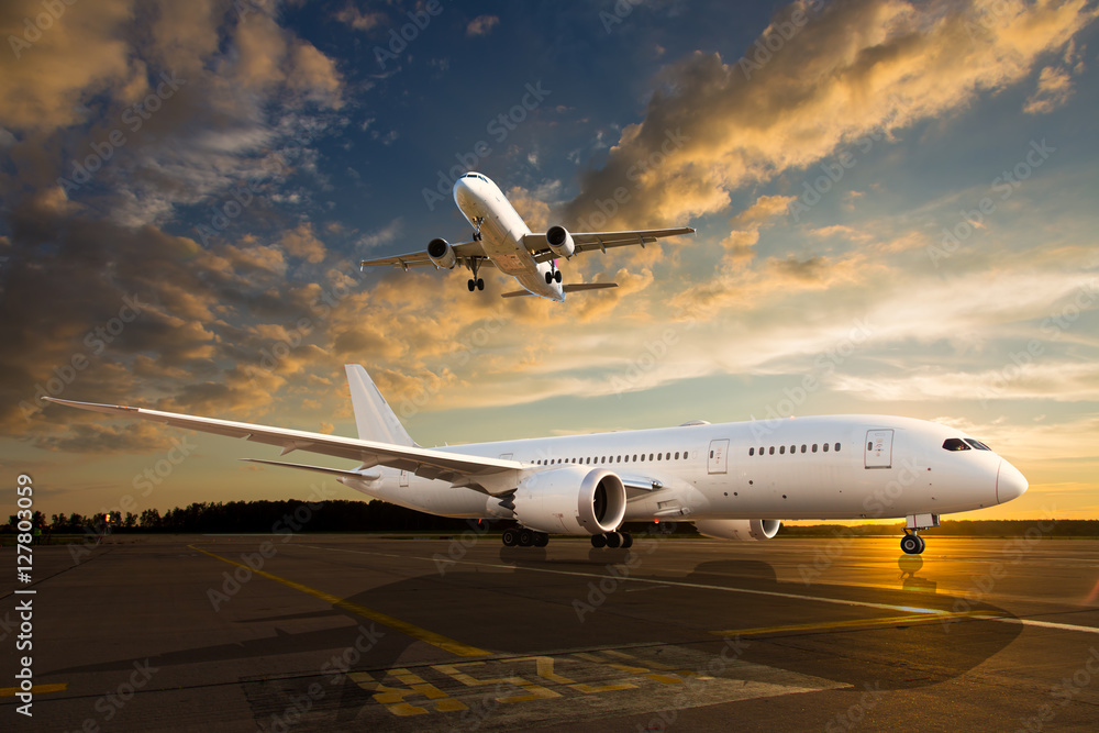 Fototapeta premium Biały samolot pasażerski na pasie startowym lotniska podczas zachodu słońca. I samoloty na niebie.