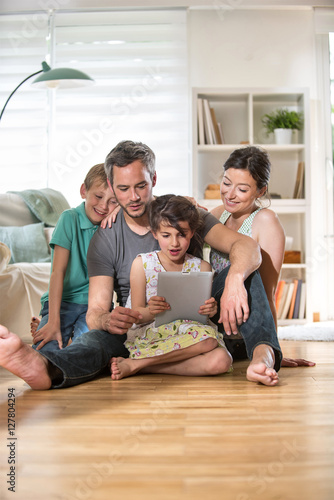 At home, a family sitting on wooden floor while using a tablet
