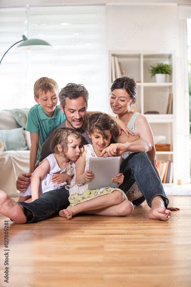 At home, a family sitting on wooden floor while using a tablet At home, a family sitting on wooden floor while using a tablet