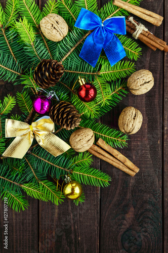 Green branch of fir, decorated with bright ribbons, balls, nuts, pine cones, cinnamon on dark wooden background. Festive composition: Christmas, New Year. The top view