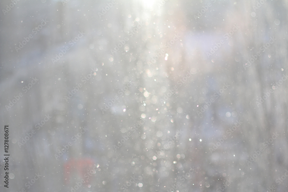 Blurred background of snowfall. Abstract silver christmas background with white lights.