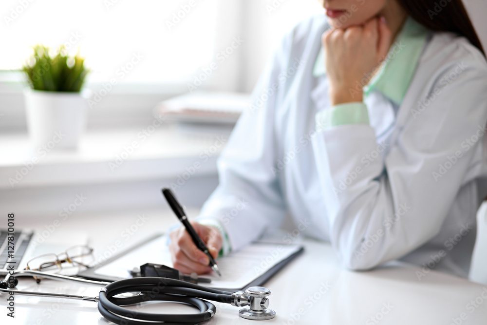 Close up of unknown female doctor sitting at the table near the window in hospital and typing at laptop computer Close up of unknown female doctor sitting at the table near the window in hospital and typing at laptop computer