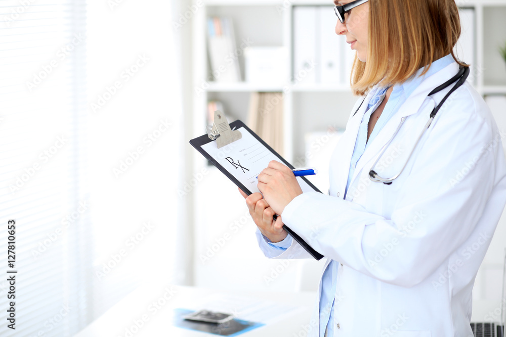 Close up of female doctor writing a medical prescription at clipboard while standing Close up of female doctor writing a medical prescription at clipboard while standing