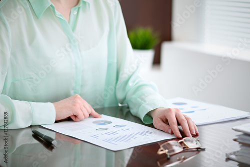 Business woman hands in a green blouse sitting at the desk in the office and examine the financial results , the right window .