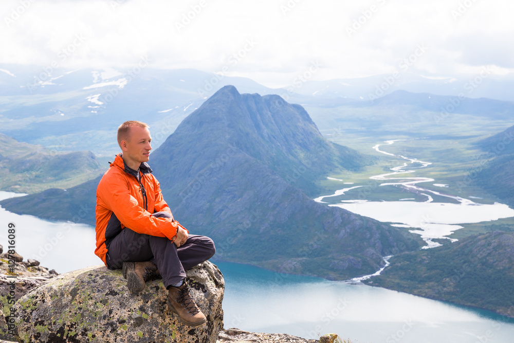 Young man hiking on Besseggen. Happy guy enjoy beautiful lake and good weather in Norway.