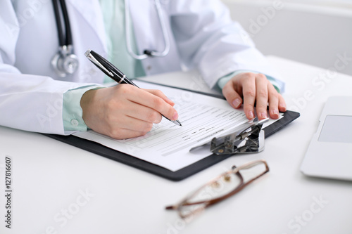 Close-up of a female doctor filling  out application form   sitting at the table in the hospital