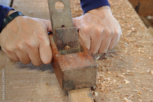 Hand of worker planing a plank of wood using a hand planer