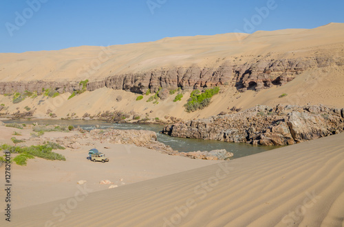 Offroad camping at Kunene River in front of towering ancient Namib Desert sand dunes of Namibia and Angola