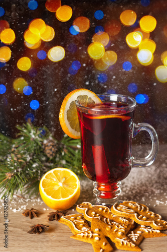 Mulled wine or hot tea, falling snowflakes, lemon, Christmas cookies and cinnamon on a background of lights