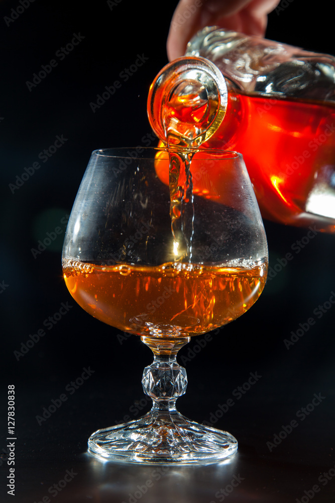 Cognac is poured from a bottle into glass Cognac is poured from a bottle into glass