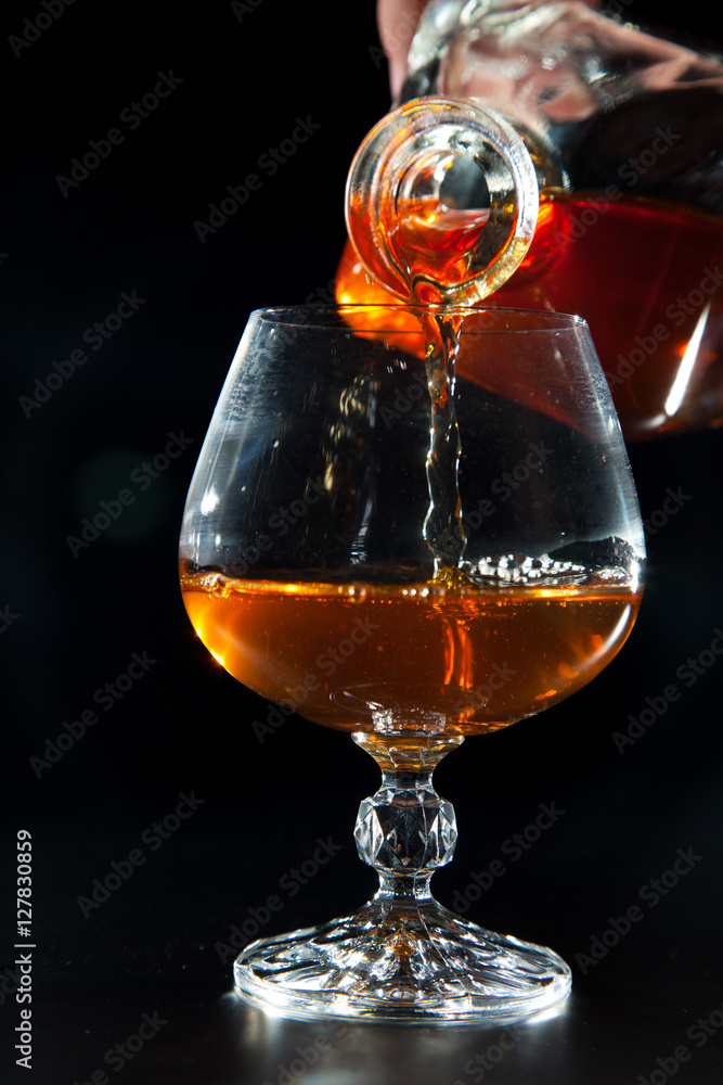 Cognac is poured from a bottle into glass Cognac is poured from a bottle into glass