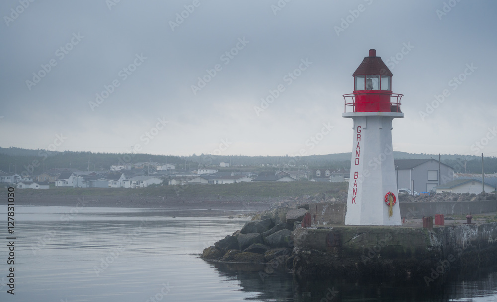Red & white lighthouse in quiet Grand Bank, Newfoundland.  Gray, overcast morning on Atlantic shoreline.  A lone lighthouse atop an outcropping of rock at the end of a pier.
