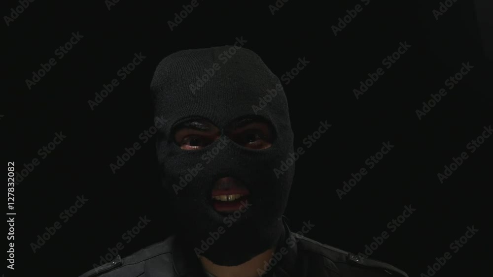 Burglar masked talking to the camera. Black background and dramatic light. Burglar masked talking to the camera. Black background and dramatic light.