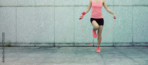 young fitness woman rope skipping against city wall